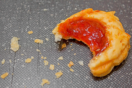 Visione parziale di un dolcetto di pasta sfoglia e marmellata di fragole, su fondo neutro.
