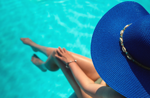 Woman in blue hat is relaxing near the pool.