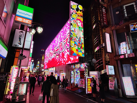 Crowd of people walking on a street surrounded by flashing neon lights in Kabukichō, an entertainment district in Shinjuku, Tokyo, Japan. Kabuki-chō is the location of many host and hostess clubs, love hotels, shops, restaurants, and nightclubs, and is often called the \