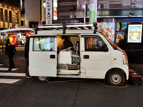 Young guy at his small food truck at night in Kabukichō, an entertainment district in Shinjuku, Tokyo, Japan. Kabuki-chō is the location of many host and hostess clubs, love hotels, shops, restaurants, and nightclubs, and is often called the \