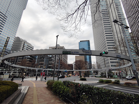 People walking at a roundabout surrounded by tall skyscrapers in Nishi-Shinjuku, Tokyo.