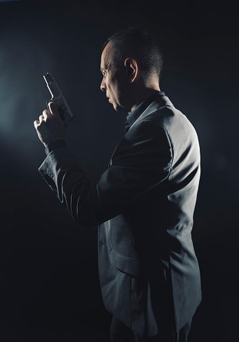 Spy in elegant suit with pistol gun in dark studio shot photo with plain background and copy space.