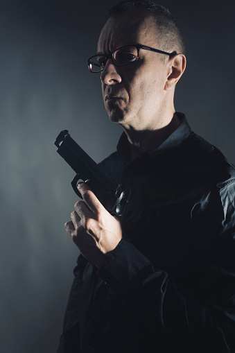 Spy thriller mafia boss assasin portrait photo in suit holding pistol gun.