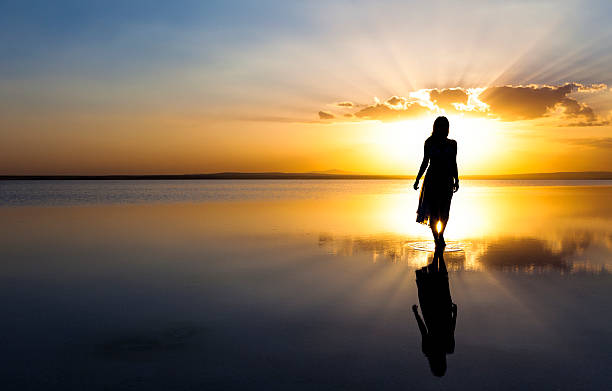 joven mujer caminando en el agua en la puesta de sol - devoto fotografías e imágenes de stock