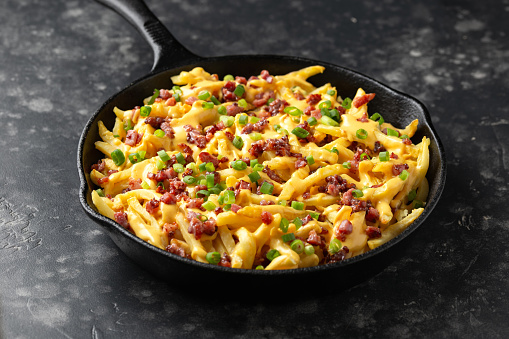 Crispy French fries loaded with bacon, cheese sauce and spring onion in iron cast pan.