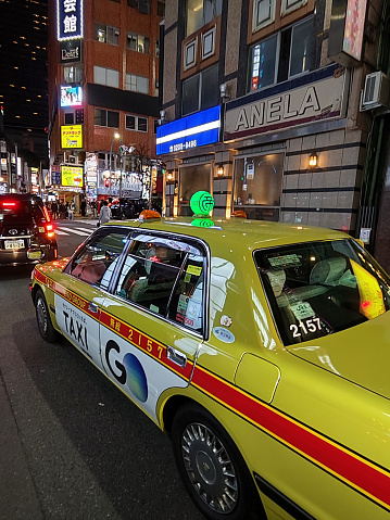 Taxi riding on a street at night in Kabukichō, an entertainment district in Shinjuku, Tokyo, Japan. Kabuki-chō is the location of many host and hostess clubs, love hotels, shops, restaurants, and nightclubs, and is often called the \