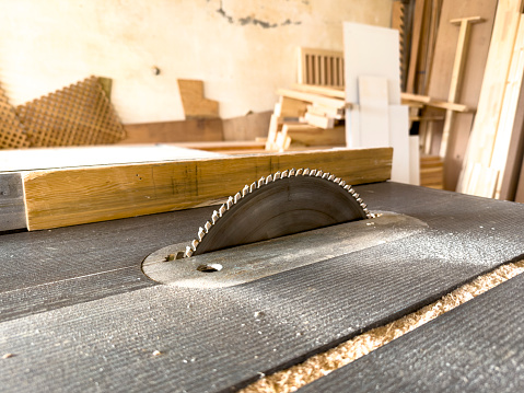 A carpenter works in a furniture workshop with various tools and a board