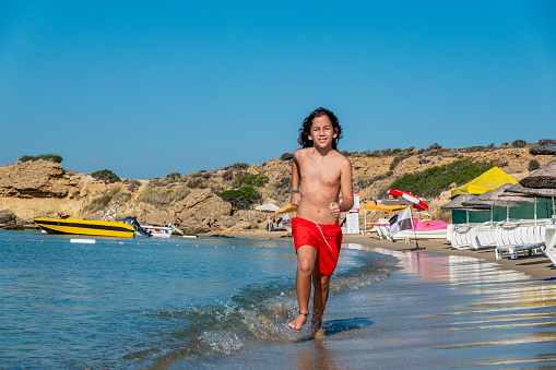 A handsome 12-year-old boy jogs along a beach on the island of Bozcaada in the North Aegean Sea on a sunny morning.