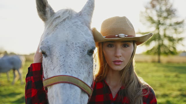 SLO MO Close-Up Portrait of Beautiful Young Cowgirl in Hat Stroking White Horse and Looking At Camera at Farm