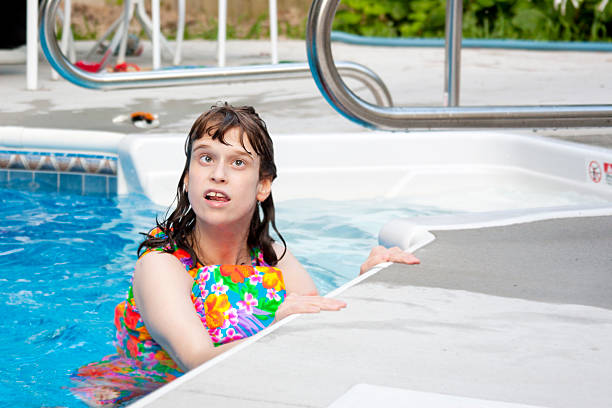 Disabled little girl wearing floatation bathing suit looks up from the side of the pool (shallow dof)