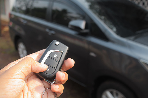 Driver pressing car lock or unlock alarm key and pointing it to his car in the background