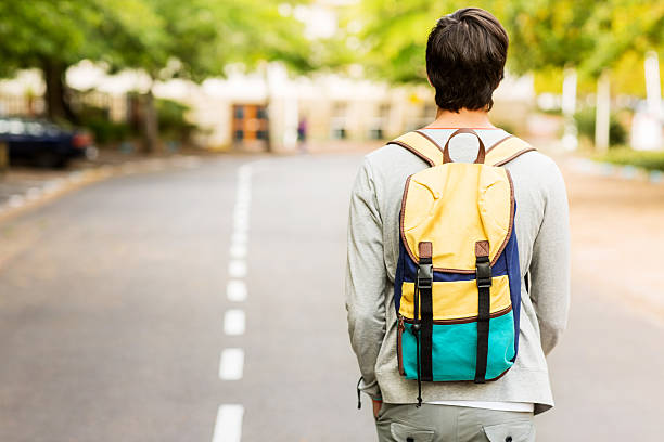 Student With Backpack Walking On Street Rear view of high school student with backpack walking on the road and looking to the future. Horizontal shot. one teenage boy only stock pictures, royalty-free photos & images