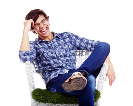 Young man in checkered shirt and blue jeans sitting in white chair with hand near his head and laughing. Isolated on white background, mask included