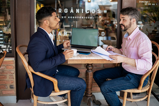 Mid adult businessman talking to business partner while going some business reports during a meeting in a coffee shop