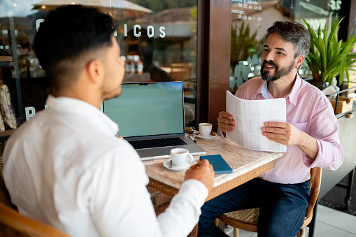 Two businessmen going over paperwork during a coffee break together in a cafe