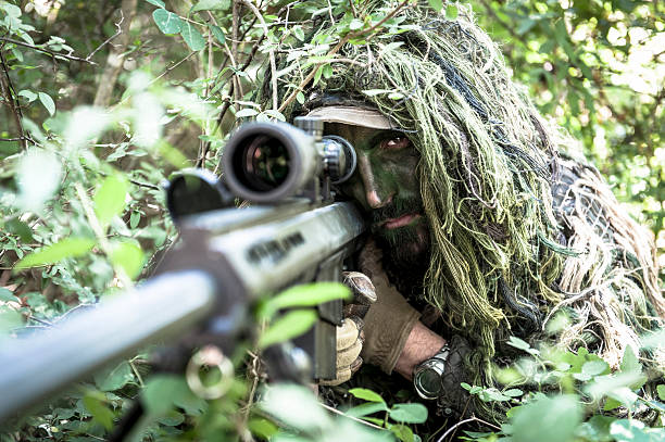 Sniper Hiding in Ghillie Suit Aiming Barrett Precision Rifle stock photo