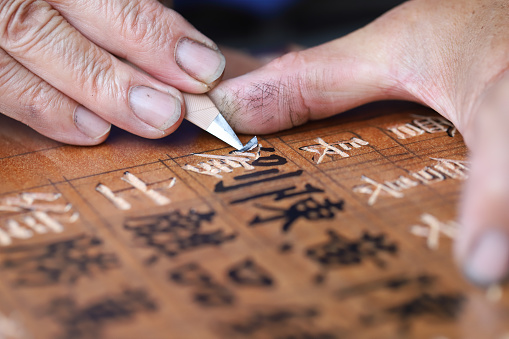 The woodcarving master is carving a plaque. \nHe carved Chinese characters on the plaque. Handmade woodcarving is one of Taiwan's traditional products. It is gradually declining, and handcarving is gradually being replaced by machine carving.