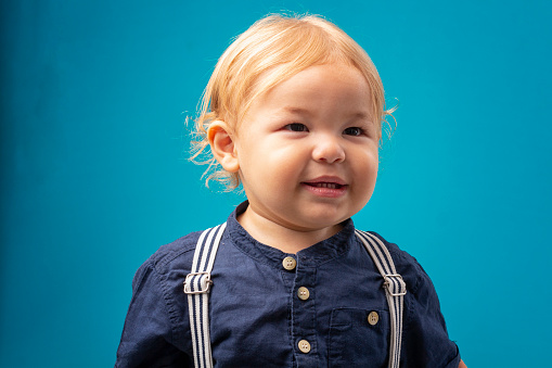 2 year old boy in studio photo with blue background smiling and posing