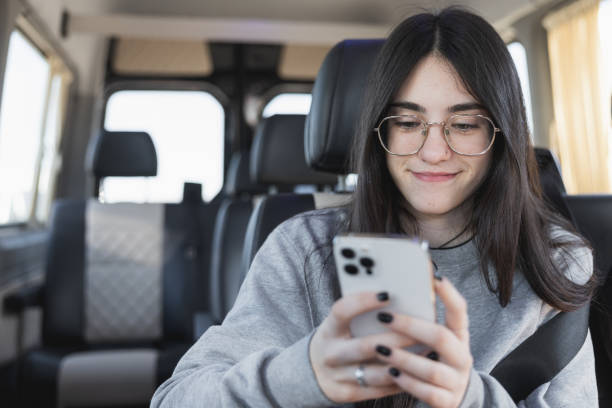 Teenage girl with glasses using smartphone inside a van. stock photo