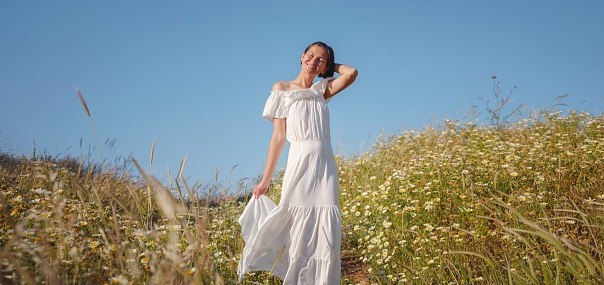 Beautiful Asian young woman in white dress outdoor in flower field. embracing fresh air and engaging in outdoor activities. Friluftsliv concept means spending as much time outdoors as possible