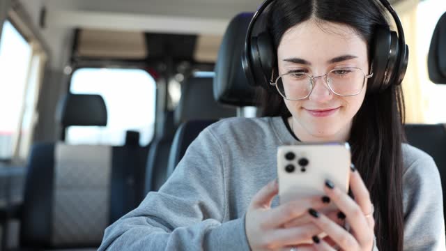 Teenage girl with glasses using smartphone inside a van.