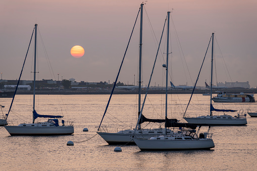 Yachts moored in the harbour near Long Wharf in the Financial District in Boston.  This is taken as the sun rises over Logan Airport.
