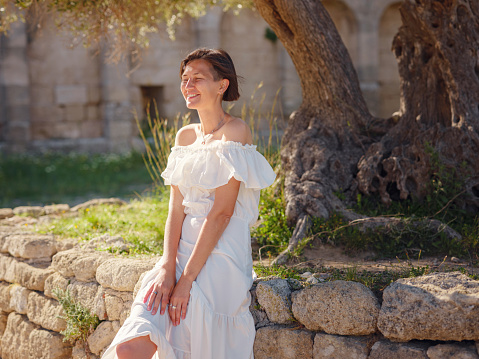 Beautiful Asian young woman in white dress outdoor. Acropolis of Rhodes Famous ruins of ancient settlement with various buildings such as stadium and theater.
