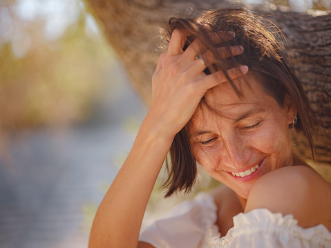 Beautiful Asian young woman in white dress outdoor near olive tree. embracing fresh air and engaging in outdoor activities. Friluftsliv concept means spending as much time outdoors as possible