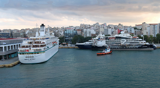 Piraeus, Greece, October 18, 2023. Large ships moored or docked at quayside jetties or piers in Port harbour. gateway to Athens. Outdoors on and autumn evening.