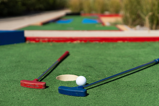 Close-up of miniature golf hole with bat and ball.