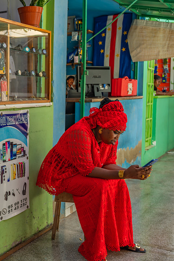 Mindelo, Sao Vicente Island, Cape Verde - October 12.2023: A women sitting with red dress and looking in the telephone in Mindelo, Cape Verde