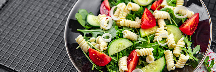 pasta salad fusilli pasta, cucumber, tomato, green lettuce, onion delicious healthy eating cooking appetizer meal food snack on the table copy space food background rustic top view keto or paleo diet vegetarian vegan food