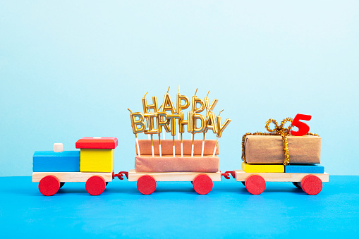 Wooden colorful toy train with Happy Birthday candles and number 5, on blue background