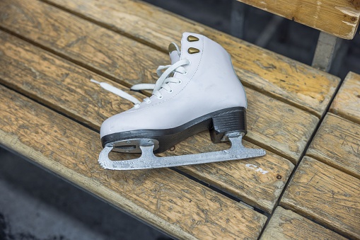 Close-up view of white figure skates resting on bench after training session at sports complex.