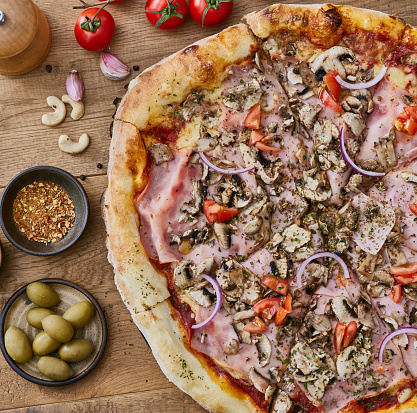 Tasty Pizza Capricciosa served on a brown rustic wooden table, representing Italian food and culture, a healthy living and healthy eating, a wellbeing and indulgence in food, enjoyment in food and street food culture lifestyle