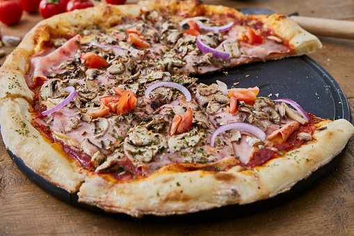 Tasty Pizza Capricciosa served on a brown rustic wooden table, representing Italian food and culture, a healthy living and healthy eating, a wellbeing and indulgence in food, enjoyment in food and street food culture lifestyle