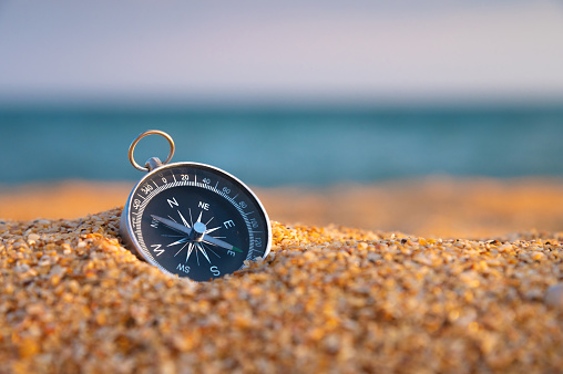 Compass on the sand close-up, sea in the background in sunset light. Finding navigation and paths. Sandy sea beach.