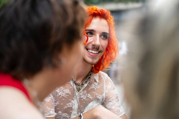 Over the shoulder view with selective focus on early 20s man with dyed red hair wearing sheer summer shirt, smiling and looking away.