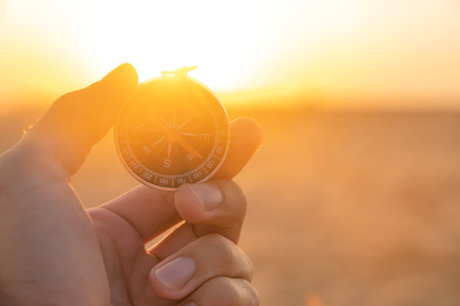hand holds a compass in the dawn light. Search concept. Sunset background.