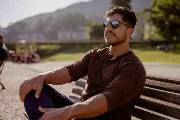 istock Smiling young man sitting outside on a park bench in summer 1776580869