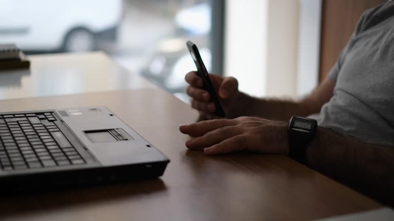 Closeup of man using smartphone with laptop