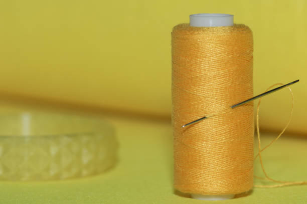 spool of yellow thread and needle on a yellow background.