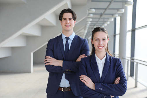 Portrait of confident business colleagues posing in office building. Young Caucasian businesswoman and businessman wearing  standing together and smiling. Team and cooperation concept