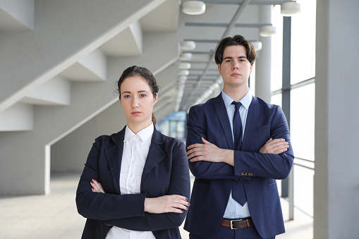 Portrait of confident business colleagues posing in office building. Young Caucasian businesswoman and businessman wearing  standing together and smiling. Team and cooperation concept