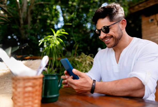 istock Smiling young man using cell phone at street cafe 1776667361