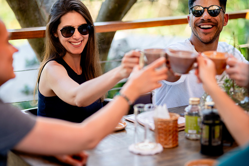 Group of friends toasting cups of coffee sitting at outdoor restaurant table