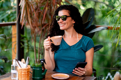 Beautiful mid adult woman sitting at outside cafe table drinking coffee