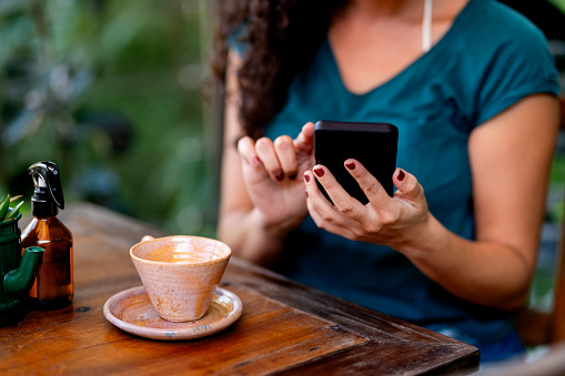 Cropped shot of a young woman using her mobile phone while sitting at outdoor coffee shop table