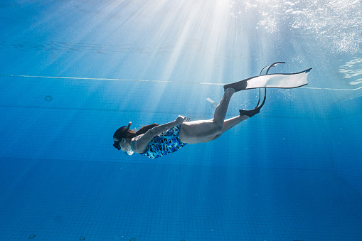 Asian women free diver alone in the depths pool. Swimmer brunette diving deep in ocean on blue underwater background. Asian women swimming underwater.