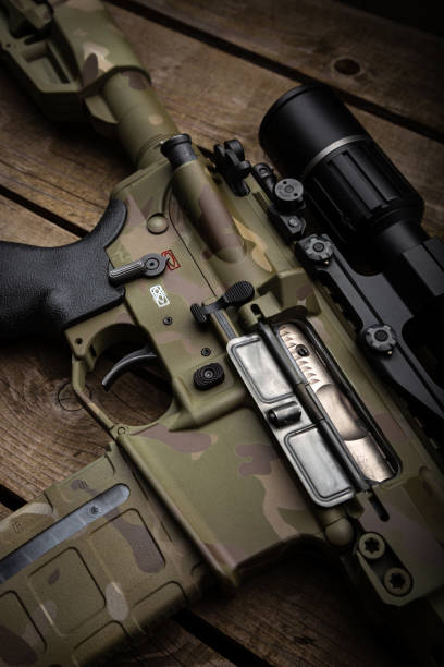 istock A modern carbine with an optical sight and a silencer. Weapons in camouflage coloring. Old wooden background. 1776690326